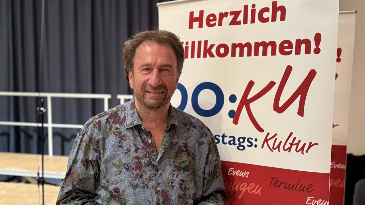 Portrait vor Plakat "Do:Ku" (Donnerstags:Kultur, eine Veranstaltungsreihe in Darmstadt)