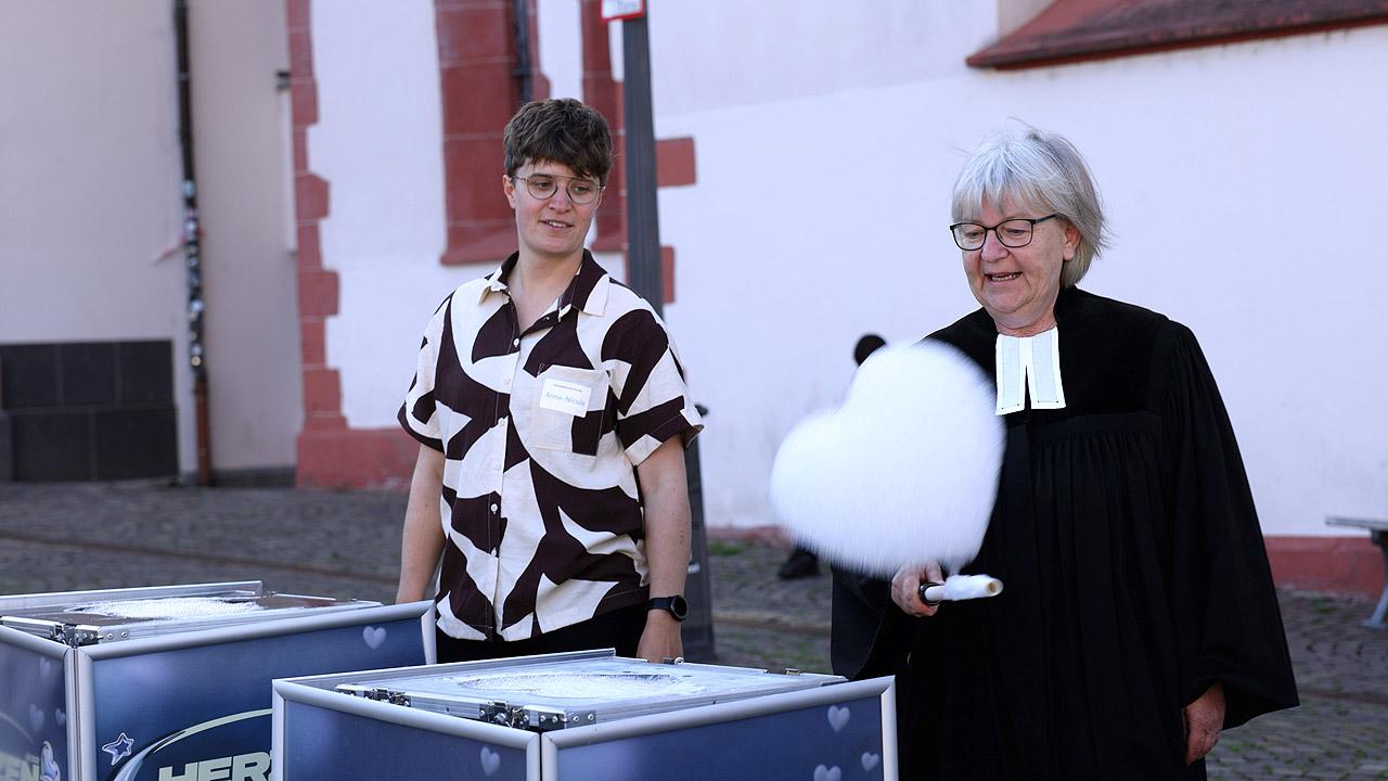 Schaumherz Zwei Personen vor einer Kirche, eine Pfarrerin lässt gerade ein Schaumherz fliegen