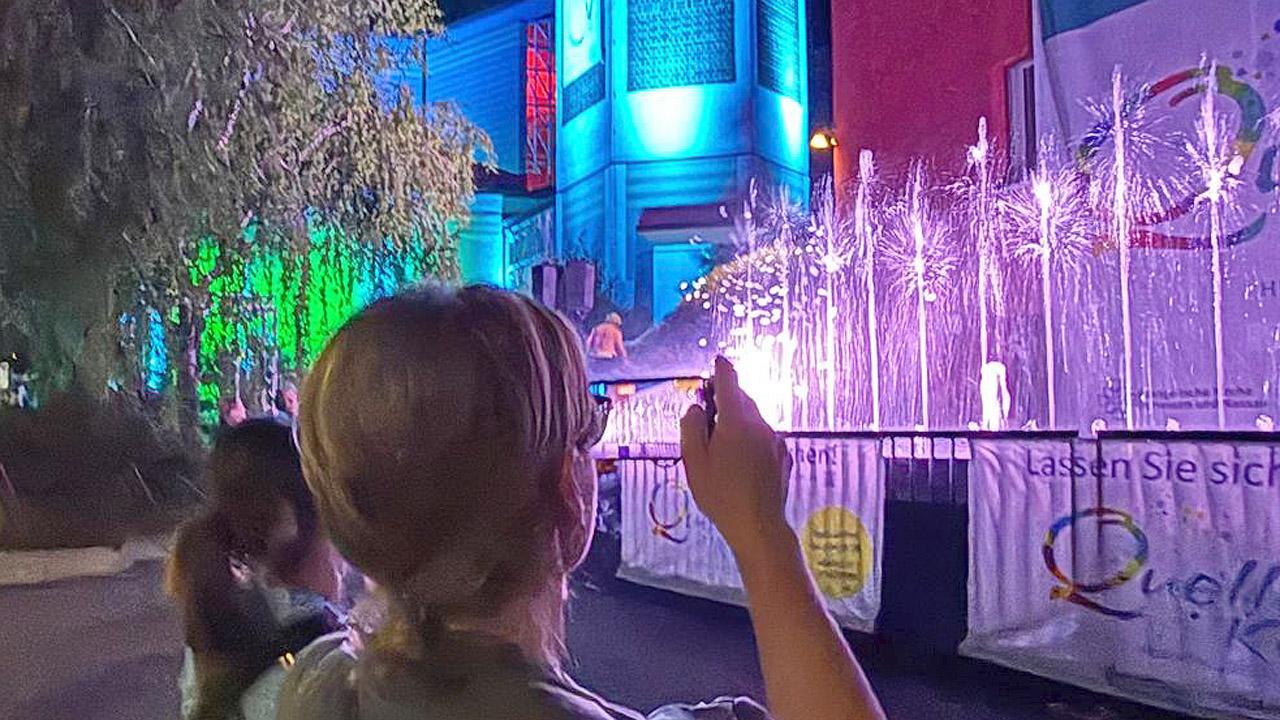 Selfie Eine Frau macht ein Handyfoto von beleuchteten Wasserfontainen