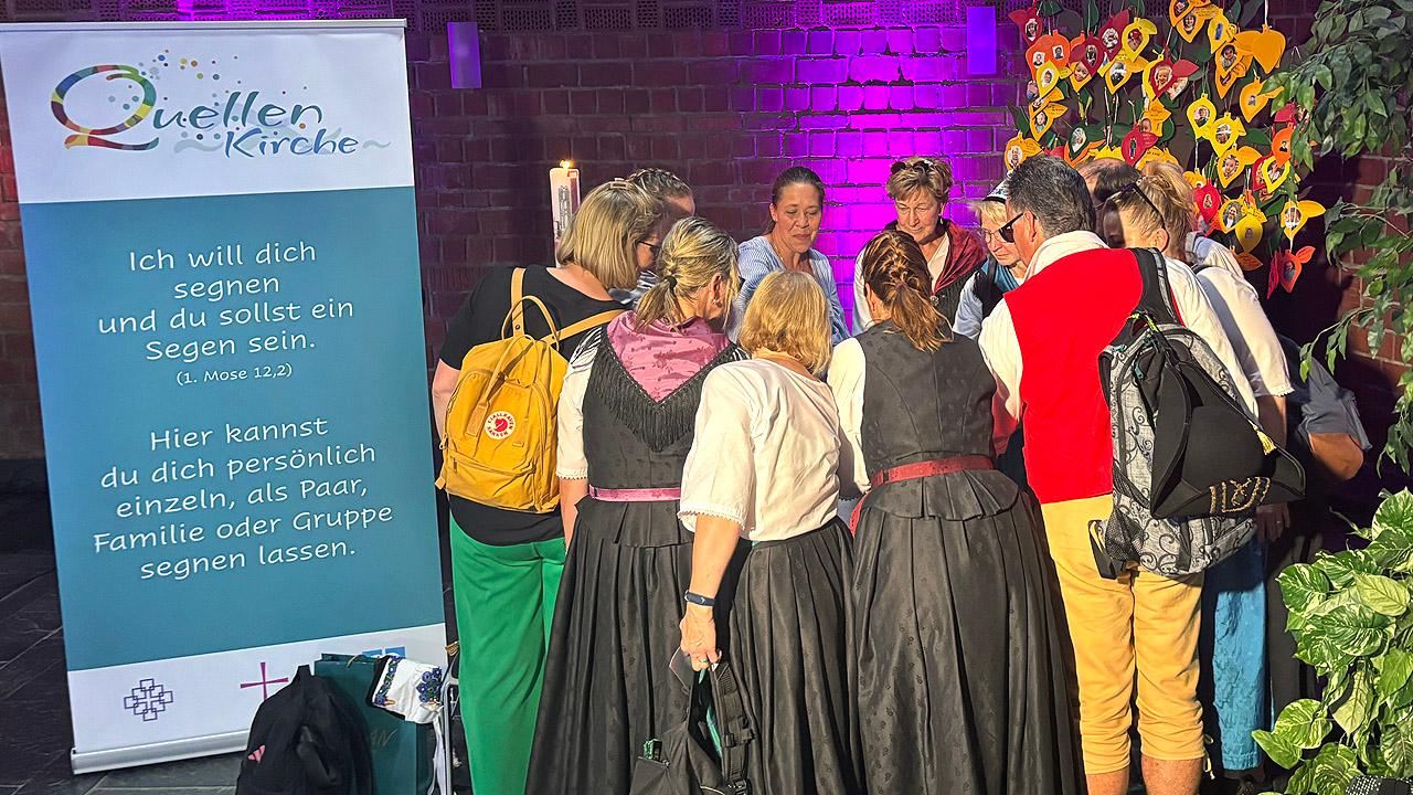 Quellenkirche Eine Gruppe von Frauen neben einem Hinweis-Rollup zur Segens-Station