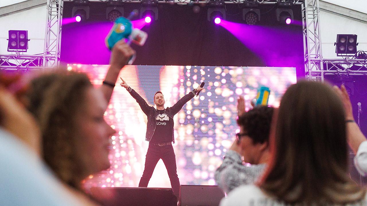 Jugendkirchentag Person auf der Bühne, die Arme und Beine ausbreitet, dahinter Lichtstrahler, von denen violettes Licht ausgeht