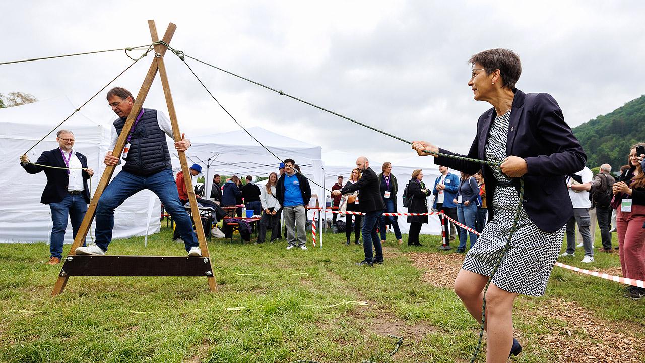 Pröpstin Sabine Bertram-Schäfer Der Kirchenpräsident balanciert auf einem Balken, die Pröpstin ist mit ihm durch ein Seil verbunden